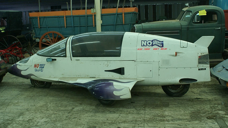 Just a land-plane in front of an Opel GT and next to a covered wagon is all